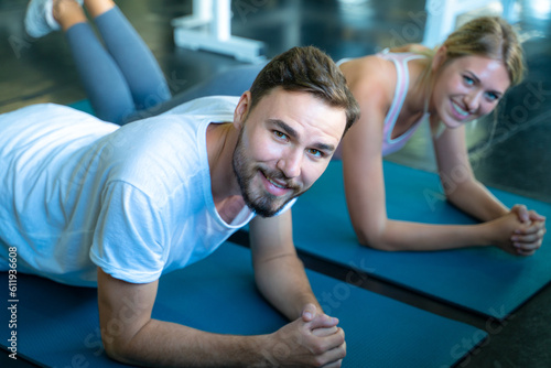 Smart man and woman buddy doing push up exercises and planking at indoor physical fitness
