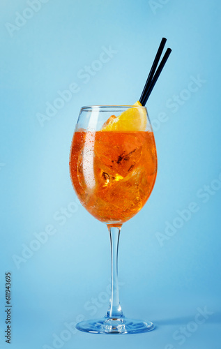 glass of aperol spritz cocktail with black straws on blue background