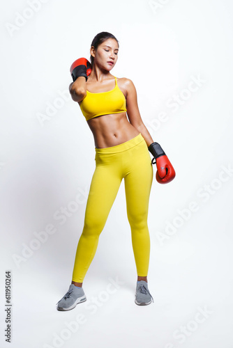 Asian woman with boxing gloves in fitness outfit while look up, isolated on yellow background.
