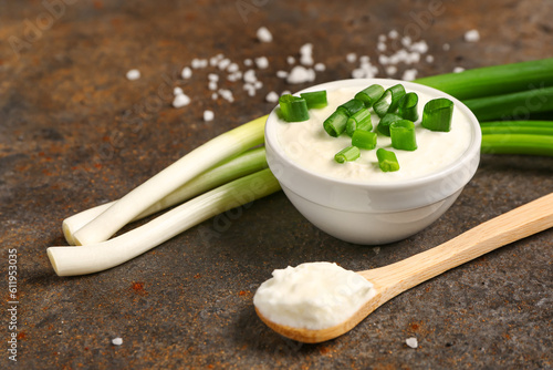 Bowl and spoon of tasty sour cream with sliced green onion on dark background