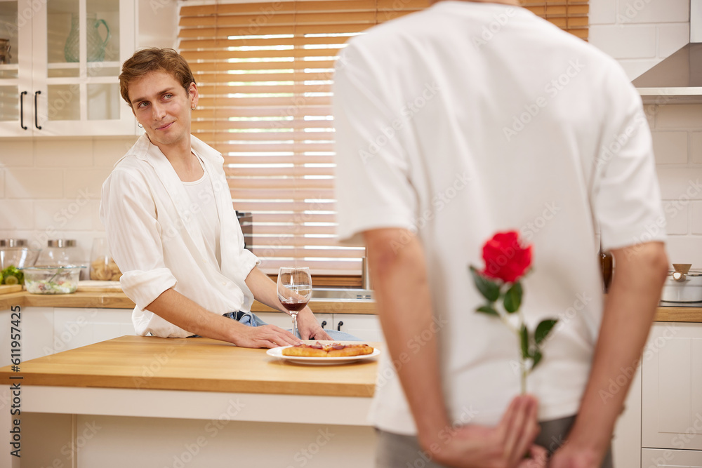 young gay couple looking at boyfriend and holding rose behind his back for surprise in the kitchen young gay couple looking at boyfriend and holding rose behind his back for surprise in the kitchen