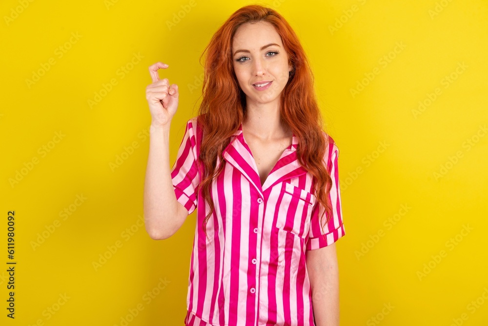 Young red haired woman wearing pink pyjama over yellow studio background pointing up with fingers number nine in Chinese sign language Jiu Young red haired woman wearing pink pyjama over yellow studio background pointing up with fingers number nine in Chinese sign language Jiu