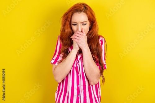 Canvas Print Young red haired woman wearing pink pyjama over yellow studio background holding
