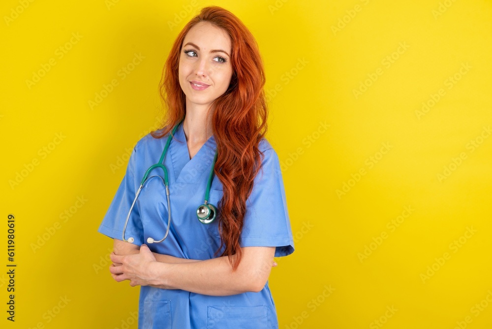 young red-haired doctor woman over yellow studio background arms crossed look empty space billboard young red-haired doctor woman over yellow studio background arms crossed look empty space billboard