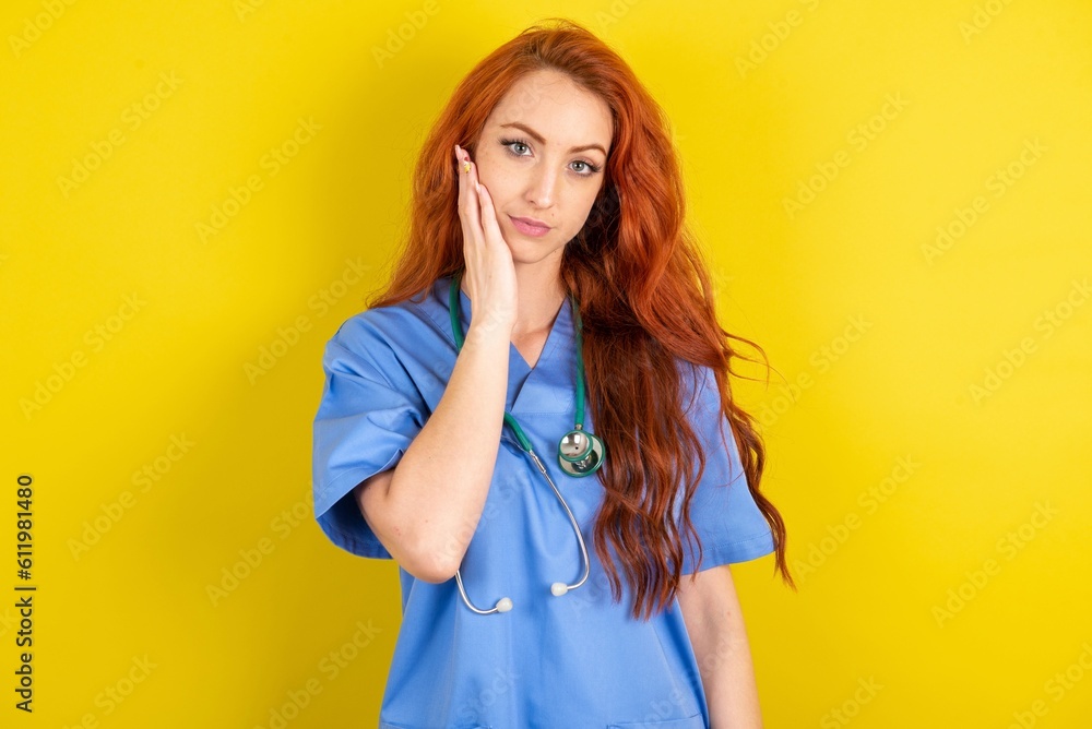 Photo of young red-haired doctor woman over yellow studio background enjoy fresh perfect smooth skin touch face Photo of young red-haired doctor woman over yellow studio background enjoy fresh perfect smooth skin touch face