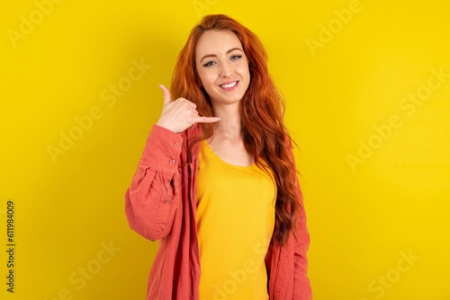 young beautiful red haired woman smiling doing phone gesture with hand and fingers like talking on the telephone. Communicating concepts.