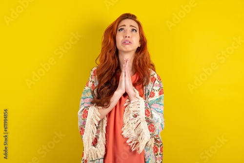 young beautiful red haired woman begging and praying with hands together with hope expression on face very emotional and worried. Please God