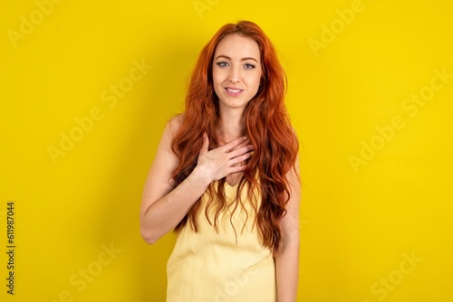 young beautiful red haired woman wearing yellow blouse over yellow studio background smiles toothily cannot believe eyes expresses good emotions and surprisement