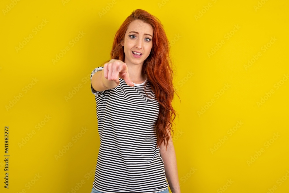 Excited positive young beautiful red haired woman wearing striped t shirt over yellow studio background points index finger directly at you, sees something very funny. Wow, amazing Excited positive young beautiful red haired woman wearing striped t shirt over yellow studio background points index finger directly at you, sees something very funny. Wow, amazing