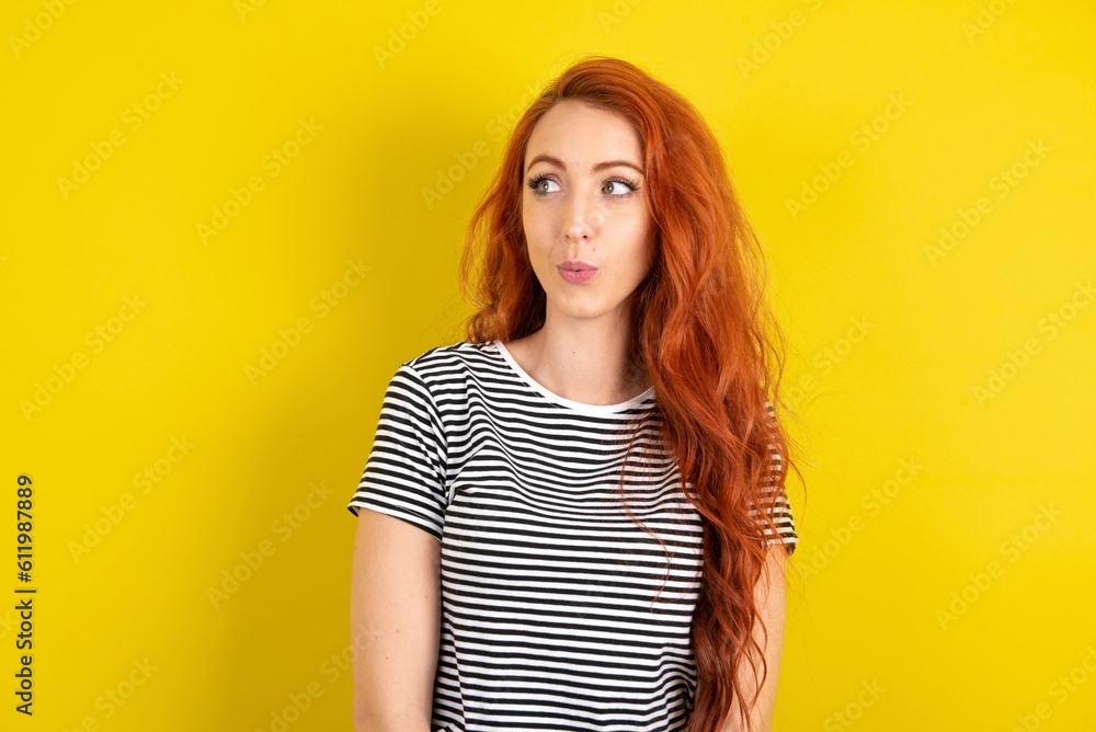 Shocked young beautiful red haired woman wearing striped shirt over yellow studio background look empty space with open mouth screaming: Oh My God! I can't believe this. Shocked young beautiful red haired woman wearing striped shirt over yellow studio background look empty space with open mouth screaming: Oh My God! I can't believe this.