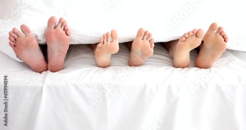 Legs of woman with two men in bed in bedroom. Polygamy in men and women