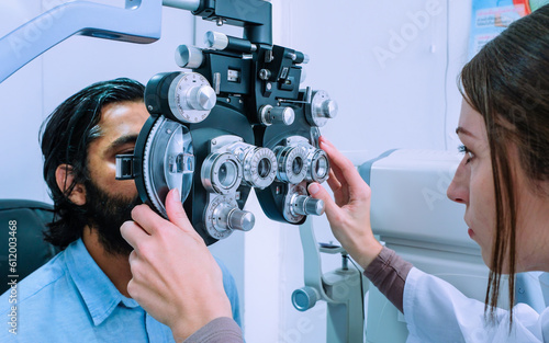 Young Caucasian woman ophthalmologist examining young man with beard with optometry for better eyesight.  Eye care concept.