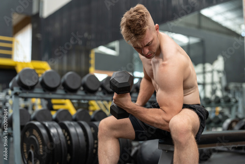 Boxer athlete man in shirtless exercising with dumbbell weights at the gym. Male with fit muscular body training and workout fitness center.