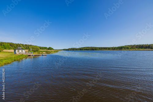 Beautiful view of landscape of nature of lake with pier for parking boat and forest trees on opposite shore. Sweden. © Alex