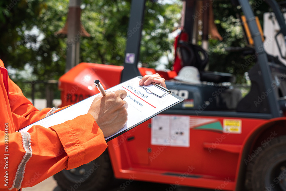 Fototapeta premium A mechanical engineer is using heavy equipment checklist form for inspecting the factory forklift vehicle (as blurred background). Industrial working with safety practice concept, selective focus. 