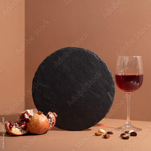 Black slate board with a glass of wine and pomegranate on beige background. Empty space for menu or recipes. Cooking or food-themed background. Round plate. Mock up template
