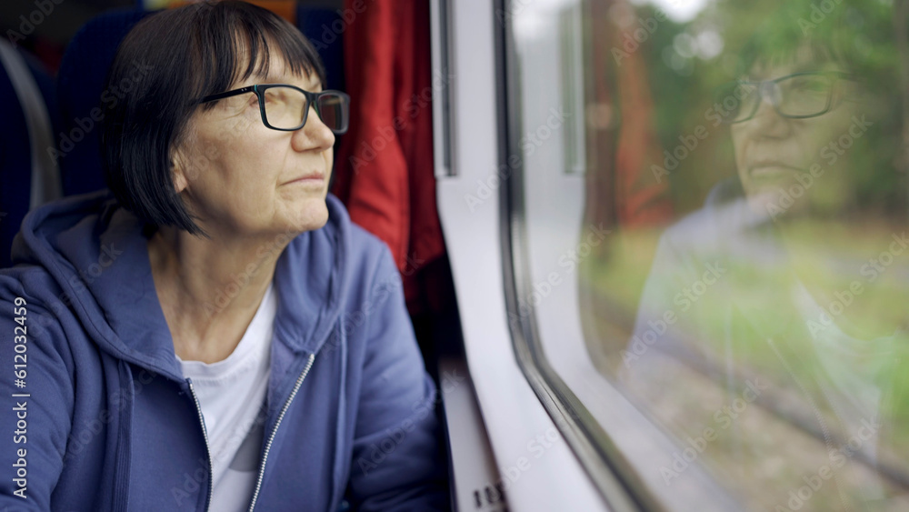 Elderly lady in glasses travels in train and looking out the window reflected in the glass Elderly lady in glasses travels in train and looking out the window reflected in the glass