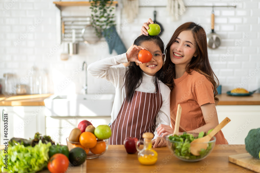 Portrait of enjoy happy love asian family mother and little asian girl daughter child having fun help cooking food healthy eat together with fresh vegetable salad and ingredient in kitchen