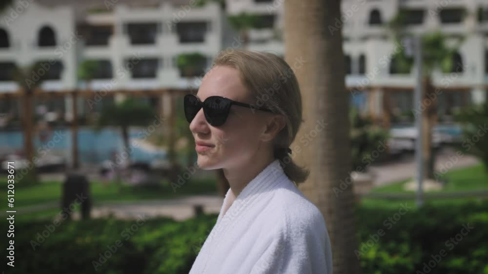 A woman in a luxury resort. A blonde woman in a white coat walks through the territory of a luxury spa hotel A woman in a luxury resort. A blonde woman in a white coat walks through the territory of a luxury spa hotel