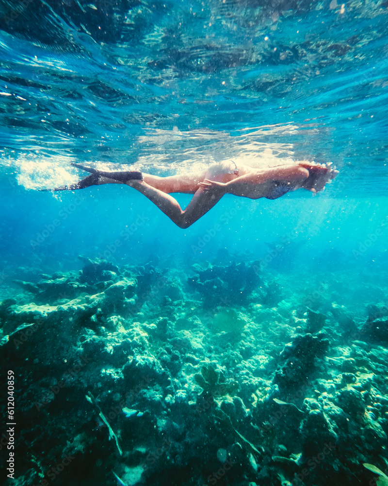A woman snorkeling over coral in blue waters