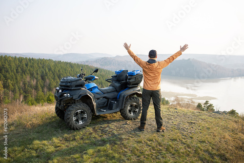 Happy man in nature standing near quad bike. Man tourist enjoying weekend activity on summer vacation.