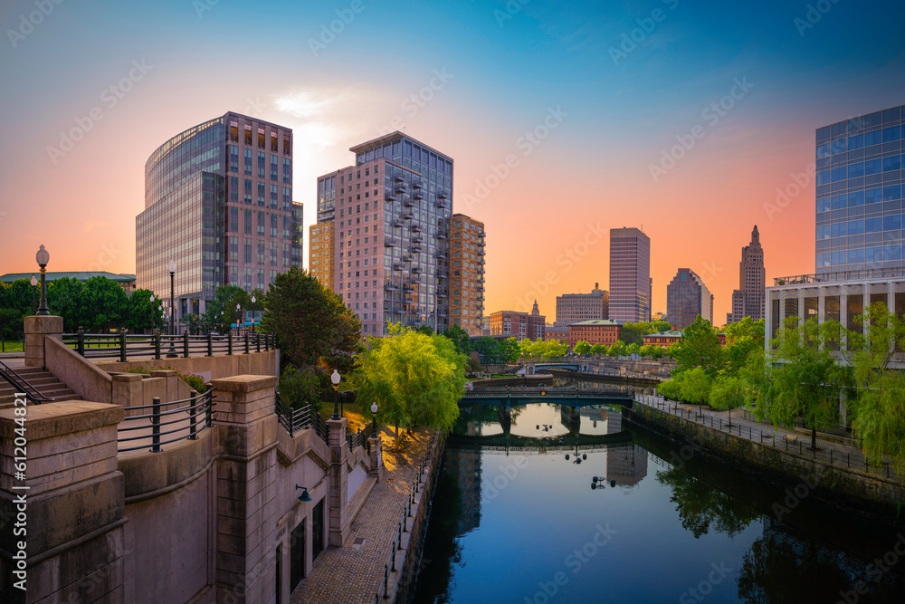 Sunrise over Providence Rhode Island. Downtown skyline, buildings, tranquil modern city park, and water reflections on the river. Glowing sunrays in the pink and blue sky.