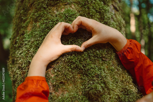 Heart hand on tree with moss, loving the nature. Hand touching a tree trunk in the forest. High quality photo