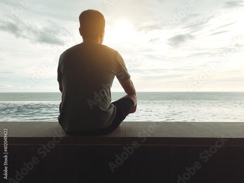 Silhouette of young man sitting and meditating with beautiful calm ocean view in early morning Travel and wellness concept