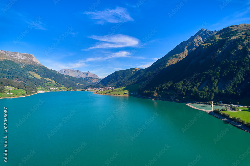 Aerial view of lake (Reschensee). Large reservoir surrounded by mountains at sunny noon. Church tower in the water. Italy, Vinschgau, Graun.