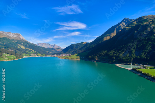 Aerial view of lake (Reschensee). Large reservoir surrounded by mountains at sunny noon. Church tower in the water. Italy, Vinschgau, Graun.