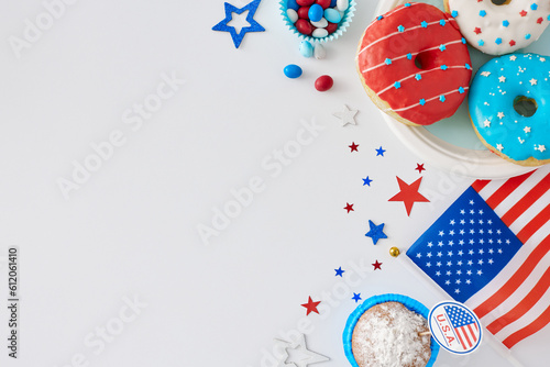 Concept of Independence Day with a sweet-filled event. Top view flat lay of american flag, donuts on the plate, muffins, candies, stars on white background with space for text or ad