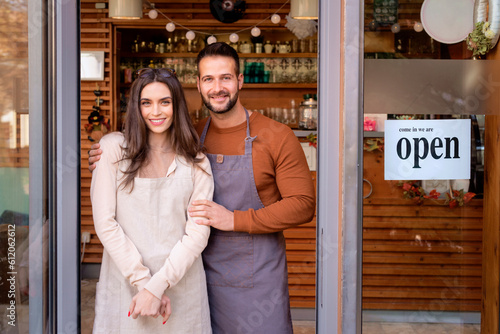 Portrait of confident female and male owners standing at entrance of cafe photo