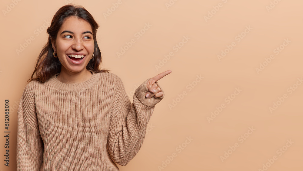 Latin woman commands attention with confident gesture pointing towards open copy space inviting viewers to embark on journey of discovery wears knitted jumper isolated over brown background. Latin woman commands attention with confident gesture pointing towards open copy space inviting viewers to embark on journey of discovery wears knitted jumper isolated over brown background.