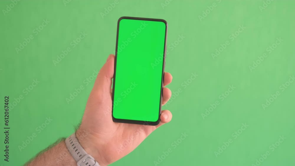Close-up slow motion of male hand swiping green smartphone screen. Hands of man holding a phone with vertical green chroma key screen. Close-up slow motion of male hand swiping green smartphone screen. Hands of man holding a phone with vertical green chroma key screen.