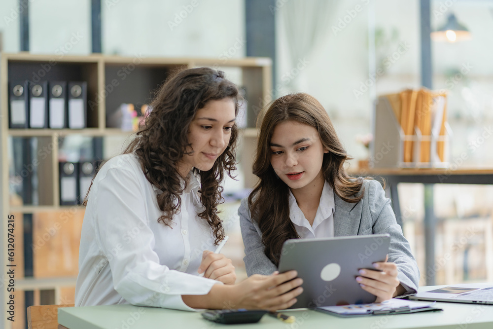 Businesswoman and accountant talking with laptop and tablet Two attractive millennial caucasian businesswoman planning project together at table in office Businesswoman and accountant talking with laptop and tablet Two attractive millennial caucasian businesswoman planning project together at table in office