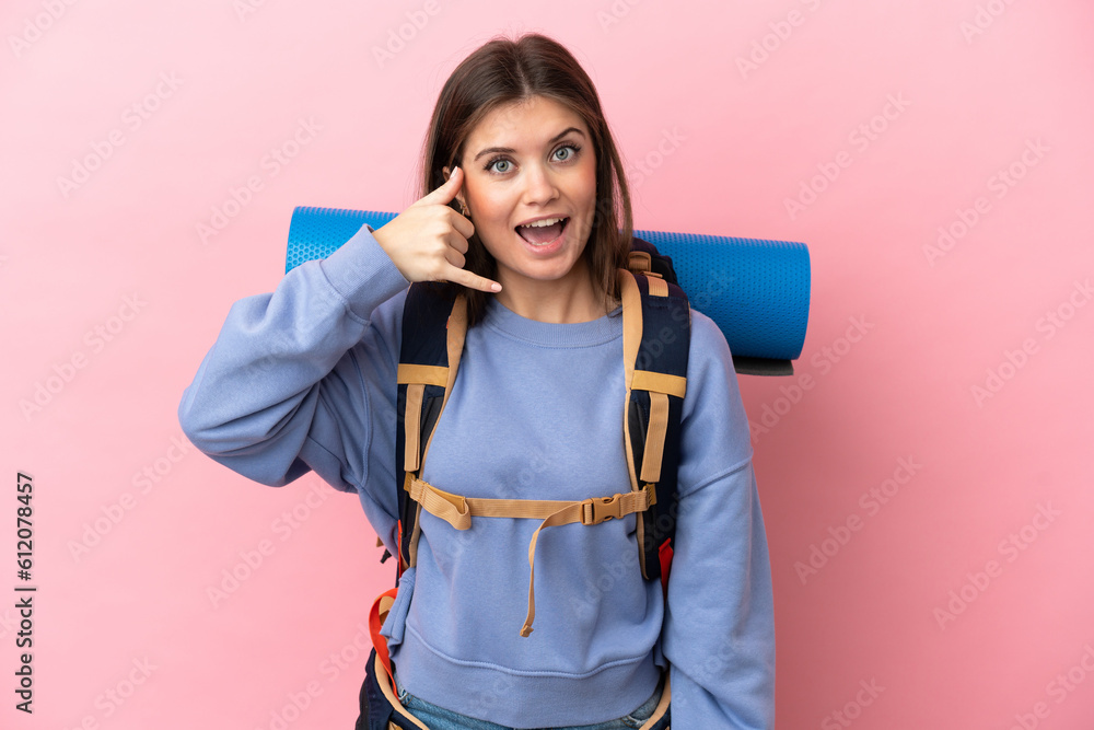 Young mountaineer woman with a big backpack isolated on pink background making phone gesture. Call me back sign Young mountaineer woman with a big backpack isolated on pink background making phone gesture. Call me back sign
