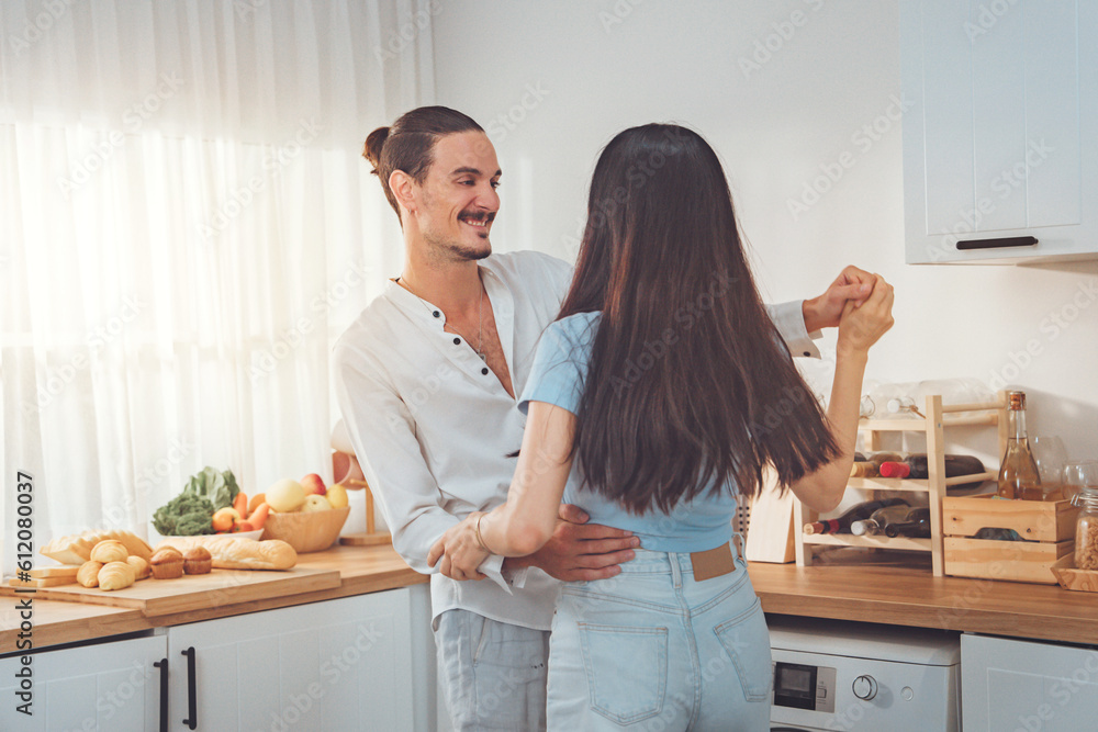 Young happy family couple dancing laughing together in kitchen at home, Cheerful husband and wife having fun moving to music in apartment.