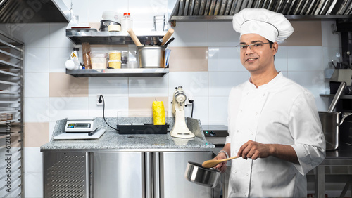 Man chef. Restaurant kitchen worker. Cook with saucepan. Cafe worker smiles and looks at camera. Indian man works as cook. Chef of confectionery shop. Cook prepares food. Horeca business