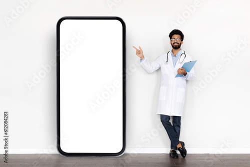 Handsome arab doctor pointing at huge smartphone with mockup