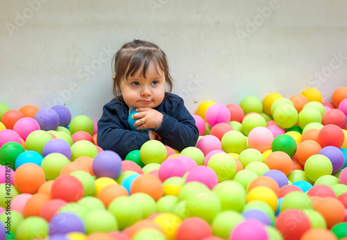 The sad little girl stand in a pool with colored balls