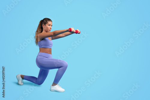 Concentrated millennial caucasian slim woman in sportswear do exercises with hand dumbbells  squats