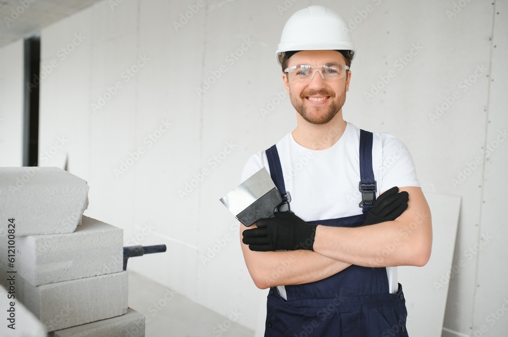 Portrait of a young foreman in uniform standing on a construction site indoors near a stepladder. Portrait of a young foreman in uniform standing on a construction site indoors near a stepladder.