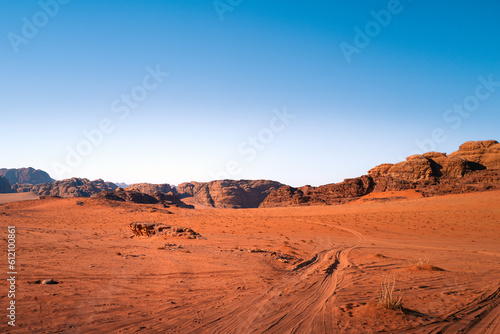 A sunny desert day in wadi rum national park, Jordan, with orange sand and tire tracks and a bright blue sky, a beautiful rocky landscape in the background and dunes in the foreground