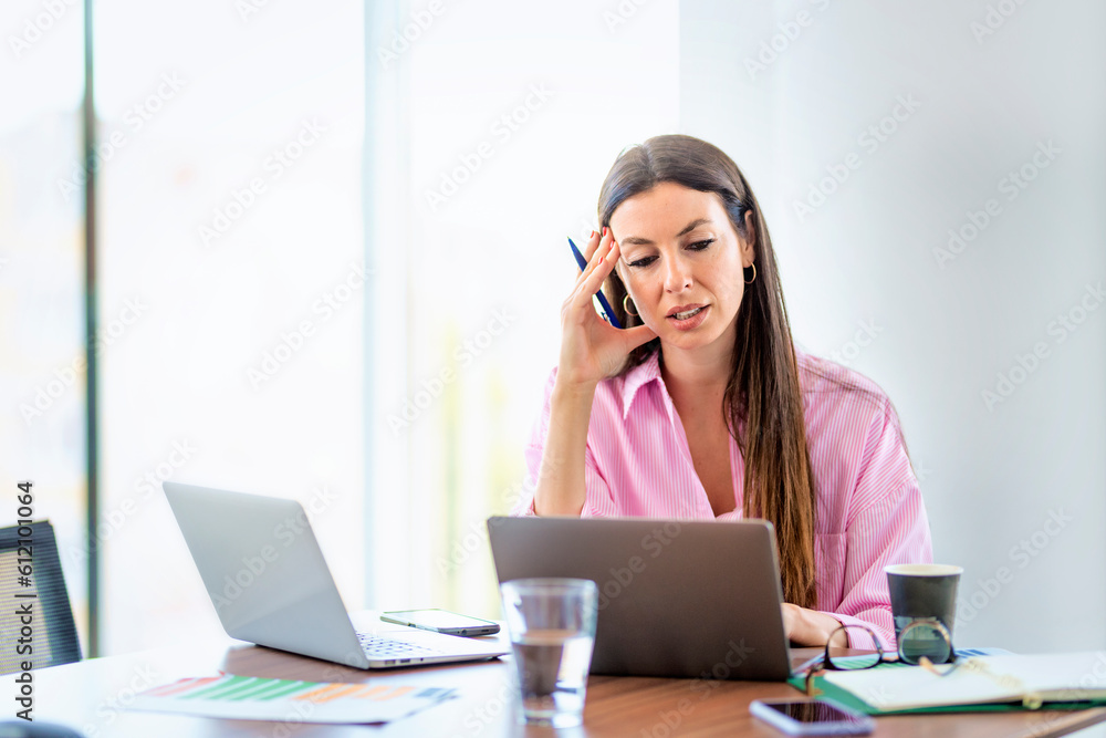 Thinking businesswoman sitting at office desk and working on laptops Thinking businesswoman sitting at office desk and working on laptops