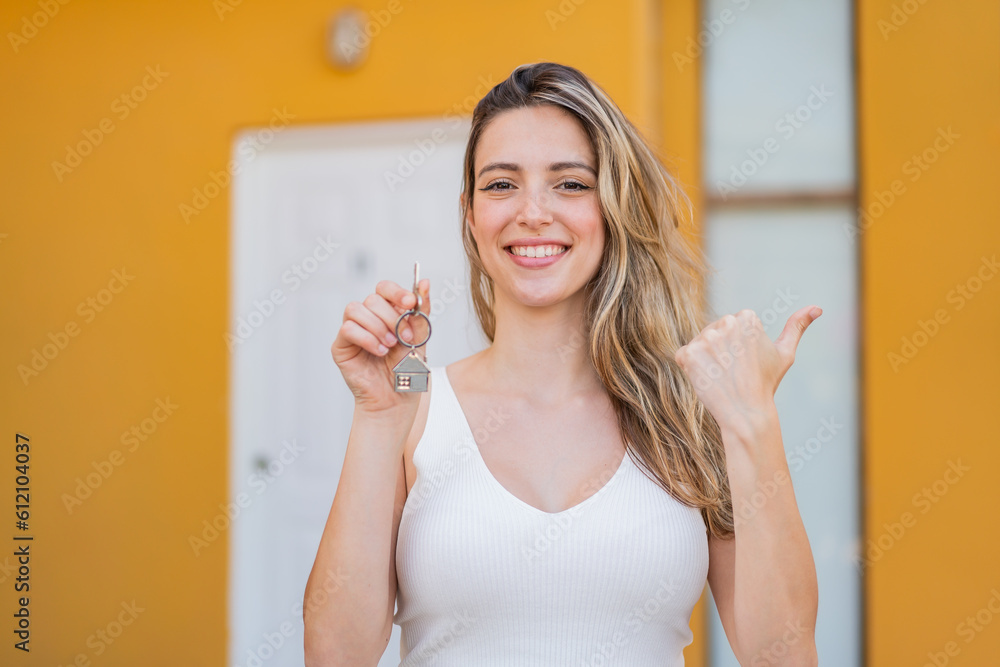 Young pretty woman holding home keys at outdoors pointing to the side to present a product Young pretty woman holding home keys at outdoors pointing to the side to present a product