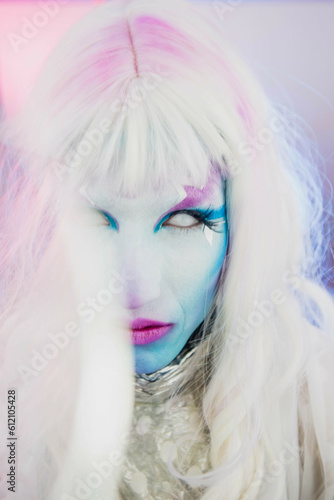 Close up on Drag queen trans person man in pink and blue light star makeup and white wig hair 