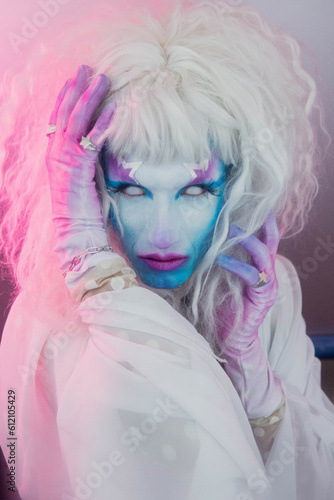 Close up on Drag queen trans person man in pink and blue light star makeup and white wig hair 