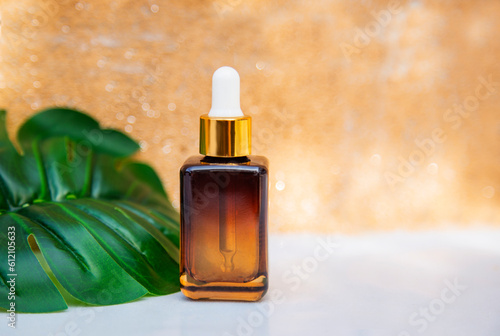 Bottle with skin care moisturizer serum on white table against brown wall background, with monstera tropical leaf. Beauty, spa and healthy lifestyle concept 