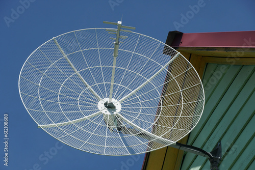 round antenna dish on the roof of the house against the blue sky