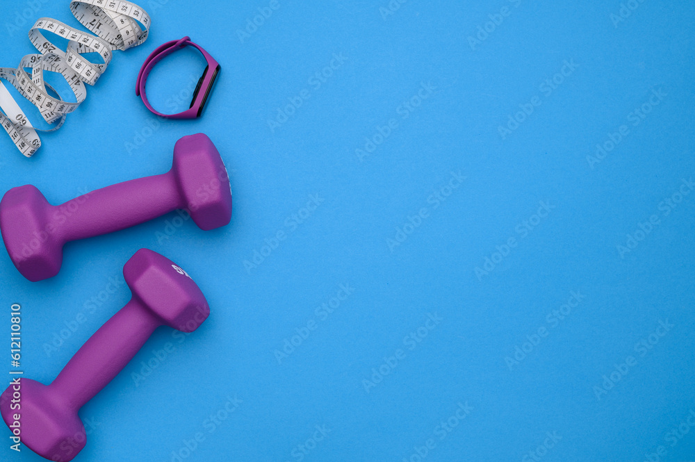Layout of two rubberized dumbbells of 2 kg of purple color,measuring tape,fitness bracelet on a blue background,top view Layout of two rubberized dumbbells of 2 kg of purple color,measuring tape,fitness bracelet on a blue background,top view